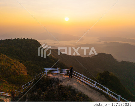 Aerial view of a traveler standing at the edge of a mountain peak viewpoint enjoying the spectacular morning mist and sunrise. 137185023
