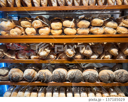 Freshly baked baguettes and artisan bread loaves displayed on wooden shelves in a bakery. Freshly baked baguettes and artisan bread loaves displayed on wooden shelves in a bakery. 137185029
