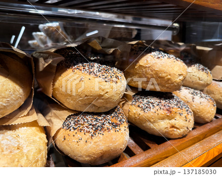 Close-up of freshly baked artisan bread rolls topped with mixed seeds in paper bags. 137185030