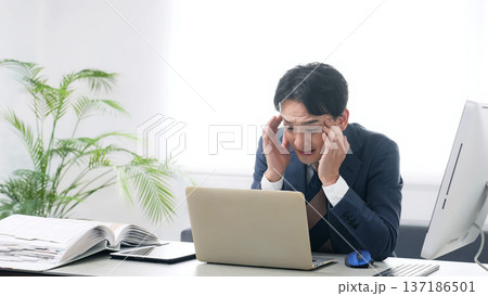 オフィスでPCを使って作業しながら悩む男性ビジネスパーソン 137186501