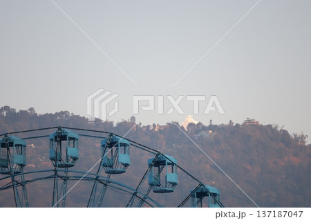 ネパールのポカラにある観覧車と山と民家と冠雪のヒマラヤ山脈の山頂と霞む空の風景 137187047