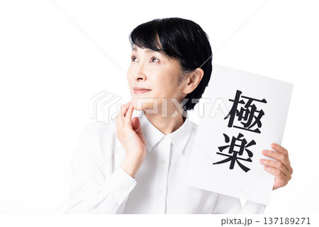 極楽と書かれた紙を持ち顎に手を添え斜め上へ視線を投げるシニア女性 137189271