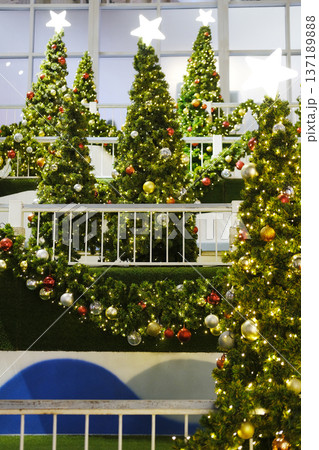 Festively decorated Christmas trees adorned with colorful ornaments and twinkling lights create a joyful holiday atmosphere in a vibrant indoor setting with greenery 137189888