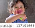 Close-up of cute curly boy enjoying exotic dragon fruit with red smudged face 137191663