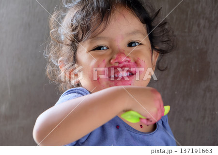 Close-up of cute curly boy enjoying exotic dragon fruit with red smudged face 137191663