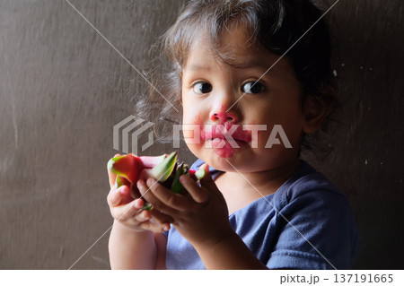 Close-up of cute curly boy enjoying exotic dragon fruit with red smudged face 137191665