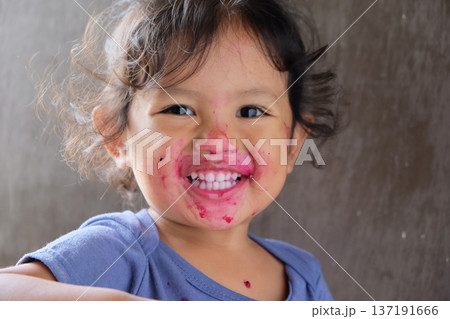 Close-up of cute curly boy enjoying exotic dragon fruit with red smudged face 137191666