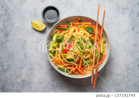 Vegetarian wok noodles with vegetables in a plate on a blue background with chopsticks 137191745
