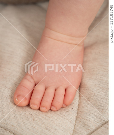 Close-up of a newborn babys foot resting on soft beige fabric. Gentle natural light and warm tones create a cozy, tender atmosphere ideal for parenting, maternity, childcare, and newborn-themed 137193749
