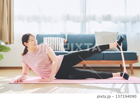 自宅でトレーニングチューブを使ってエクササイズをする30代女性のウェルネスライフ 自宅でトレーニングチューブを使ってエクササイズをする30代女性のウェルネスライフ 137194090