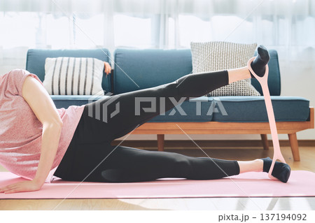 ヨガマットの上でトレーニングチューブを使い下半身トレーニングをする女性 137194092
