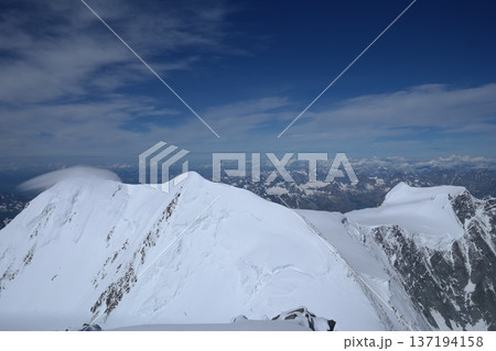 A stunning rock formation covered in snow, set against a clear blue sky with fluffy clouds in the background, creating a peaceful and breathtaking mountain landscape. 137194158