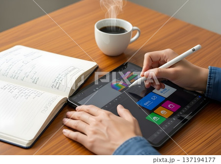 Close-up of hands using digital stylus on tablet with coffee and notebook in natural light, showing digital productivity tool in teleworking setup 137194177