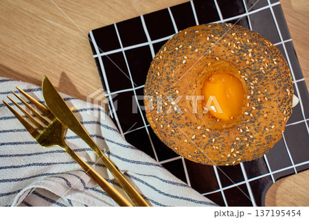 Seeded bagel with egg yolk on grid cutting board top view Seeded bagel with egg yolk on grid cutting board top view 137195454