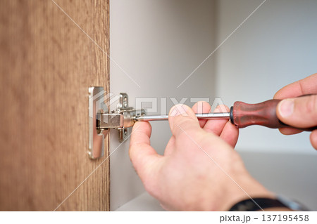 Adjusting cabinet door hinge with screwdriver 137195458