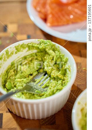 Mashed avocado in ramekin with fork on wooden cutting board 137195601