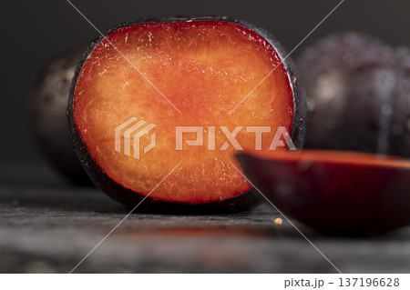 sliced black fresh juicy plums on the table, some beautiful pure black plums on the table, plum with red juicy sweet flesh cut into pieces 137196628