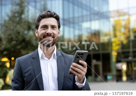 Executive man networking and communicating using a mobile phone, representing remote work, smart technology, and corporate communication in a professional outdoor setting 137197819