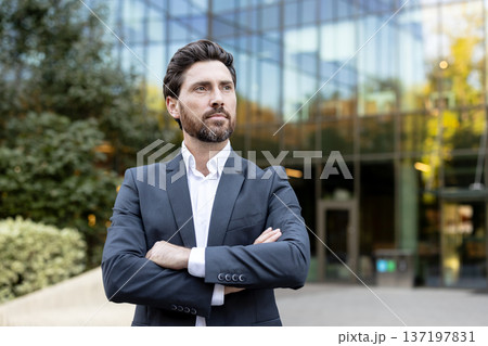 Confident businessman standing with folded arms outdoors, looking away with a thoughtful expression, representing leadership, success, and professional vision in a corporate urban setting Confident businessman standing with folded arms outdoors, looking away with a thoughtful expression, representing leadership, success, and professional vision in a corporate urban setting 137197831