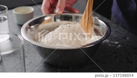 man mixing dry ingredients with flour in steel bowl on concrete countertop man mixing dry ingredients with flour in steel bowl on concrete countertop 137198054