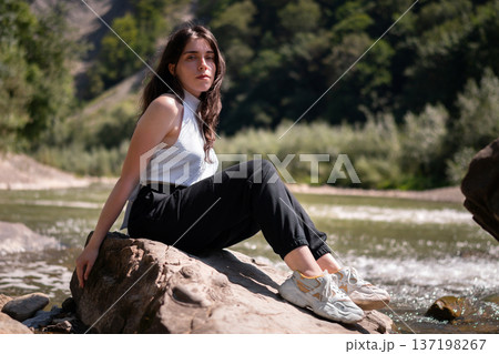 Relaxed Young Woman Resting on Rocks by a Mountain River Relaxed Young Woman Resting on Rocks by a Mountain River 137198267