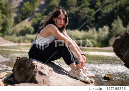 Relaxed Young Woman Resting on Rocks by a Mountain River 137198268