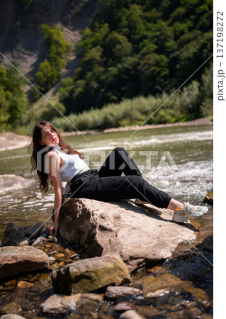 Relaxed Young Woman Resting on Rocks by a Mountain River 137198272