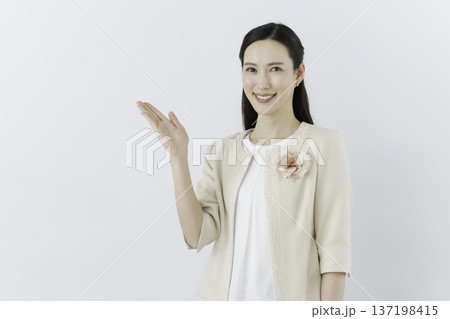 白背景の白いブラウスにクリーム色のジャケットを着て胸に花のコサージュをつけて手をかざす女性 137198415