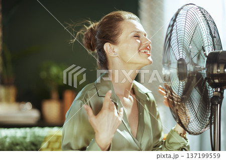 Smiling Woman Enjoying Cooling Breeze from Fan Smiling Woman Enjoying Cooling Breeze from Fan 137199559