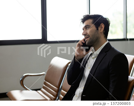 Businessman talking on smartphone while sitting in waiting area, professional communication concept, corporate lifestyle, mobile business call, modern office environment Businessman talking on smartphone while sitting in waiting area, professional communication concept, corporate lifestyle, mobile business call, modern office environment 137200803