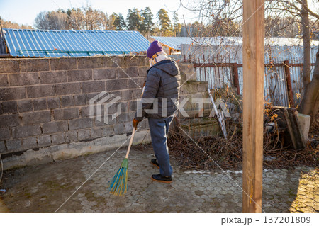 Man sweeping paved yard with broom. Cleaning outdoor area. Manual labor and maintenance at home. Housekeeping chore. Man sweeping paved yard with broom. Cleaning outdoor area. Manual labor and maintenance at home. Housekeeping chore. 137201809