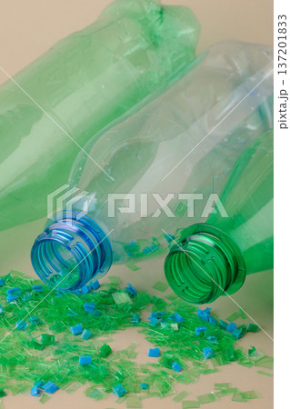 Empty plastic bottles spilling colorful crushed microplastic flakes illustrate the process of recycling and material recovery. Circular economy, green technologies 137201833