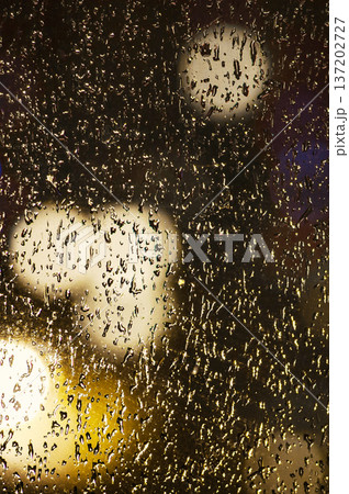 Drops on glass. Raindrops on a window against the backdrop of city lights at night. Drops on glass. Raindrops on a window against the backdrop of city lights at night. 137202727