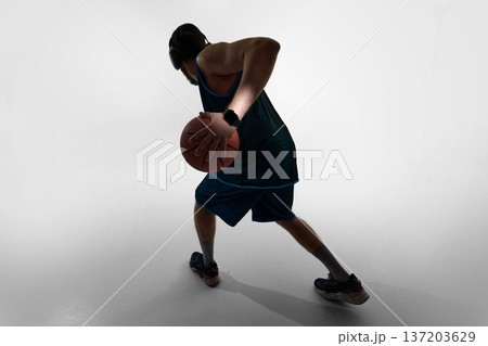 Basketball player holding ball behind back with smartwatch in studio. Basketball player holding ball behind back with smartwatch in studio. 137203629