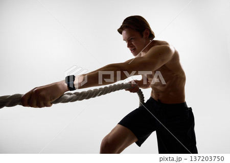 Man training with battle ropes wearing smartwatch in studio. 137203750