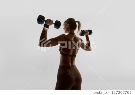 Back view of woman lifting dumbbells wearing smartwatch in studio. 137203769