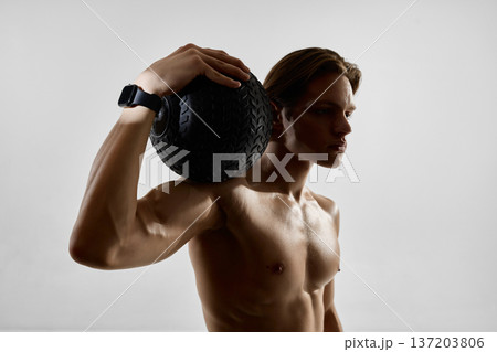 Muscular man holding medicine ball on shoulder wearing smartwatch in studio 137203806