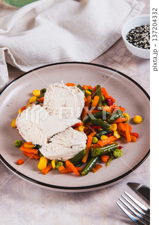 Chicken fillet and mexican mixed vegetables steamed on a plate on the table vertical view Chicken fillet and mexican mixed vegetables steamed on a plate on the table vertical view 137204332