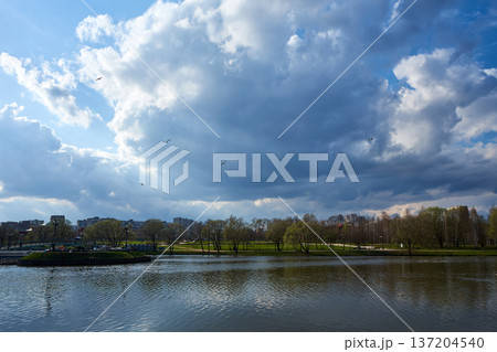 Landscape of urban park with lake and large clouds in blue sky. Nature background. Relaxing view for tranquil scenes Landscape of urban park with lake and large clouds in blue sky. Nature background. Relaxing view for tranquil scenes 137204540