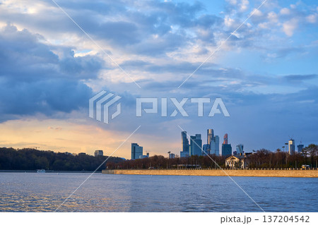 View of Moscow City from the Vorobyovy Gory pier on Moskva river with skyscrapers on the horizon under a cloudy sky. Cityscape architecture at sunset 137204542