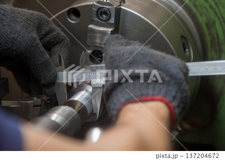 In-process dimensional inspection of a machined metal shaft using a vernier caliper by a skilled machine operator on a lathe. In-process dimensional inspection of a machined metal shaft using a vernier caliper by a skilled machine operator on a lathe. 137204672