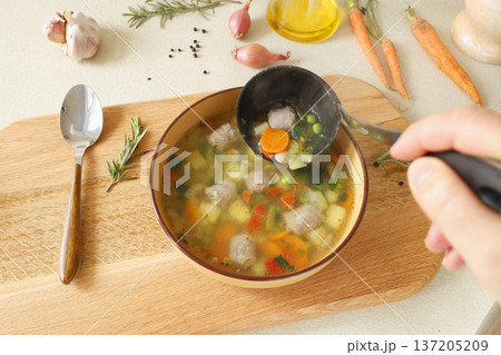 Traditional Italian minestrone soup with vegetables, sausage, served in clay bowl on wooden board. Food and healthy lifestyle. Mediterranean cuisine. Traditional Italian minestrone soup with vegetables, sausage, served in clay bowl on wooden board. Food and healthy lifestyle. Mediterranean cuisine. 137205209