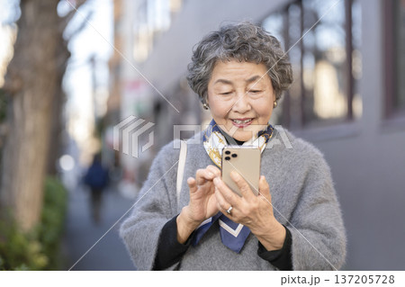 街中でスマートフォンを操作する笑顔のシニア女性 137205728