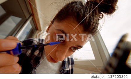 Female model crafting makeup look using smartphone camera under morning sun 137205892
