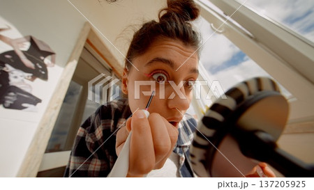 Woman carefully experiments with eyelash tools in natural light 137205925