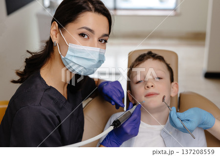 Kid in dental office. Dentist doing hygienic teeth cleaning to a boy sitting in a chair Kid in dental office. Dentist doing hygienic teeth cleaning to a boy sitting in a chair 137208559