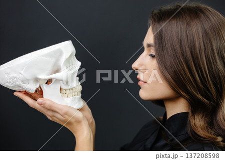 Young attractive woman doctor holding a human skull skeleton model in hands 137208598