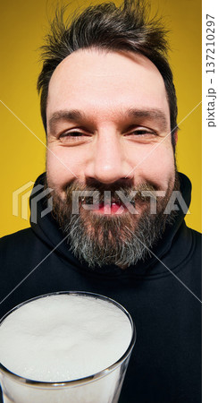 Smiling bearded man holding large beer glass close up portrait against yellow background. Smiling bearded man holding large beer glass close up portrait against yellow background. 137210297