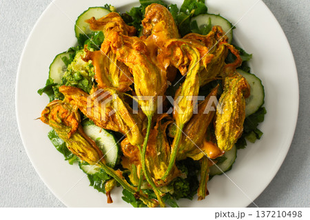 Roasted zucchini flowers sit on a bed of salad made with fresh greens, cucumbers, and broccoli. This dish highlights summer flavors and healthy eating options Roasted zucchini flowers sit on a bed of salad made with fresh greens, cucumbers, and broccoli. This dish highlights summer flavors and healthy eating options 137210498