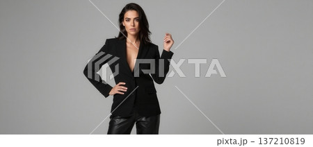 Elegant Brunette Woman in Stylish Black Blazer and Leather Pants Posing Against Grey Studio Background 137210819